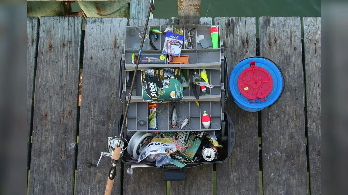 Geöffnete Tackle-Box mit Kunstködern, Rute und Köderdose